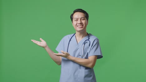 médico masculino asiático con estetoscopio sonriendo y señalando al lado en el fondo de la pantalla verde en el hospital