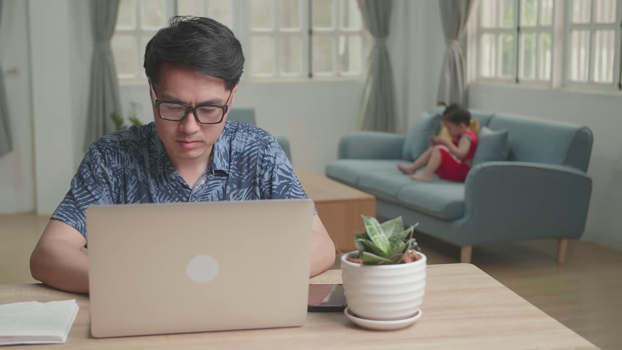 Asian Man Working With Laptop Computer And His Son Watching On Mobile Phone , Video In 4K