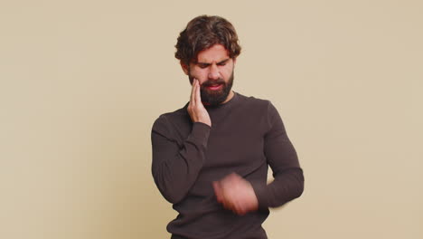 young indian bearded man touching sore cheek suffering from toothache cavities on beige background