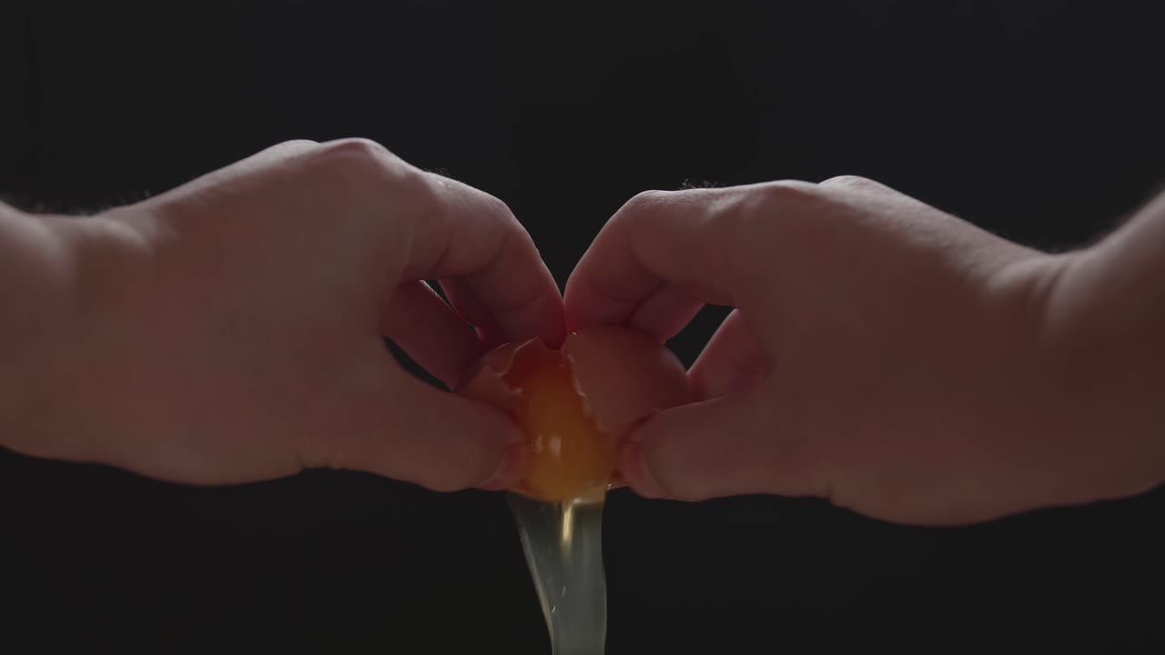 Breaking An Egg.Hands Holding A Cracked Egg.Black Background