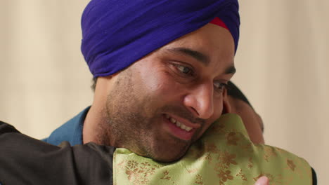 a man with a blue turban smiles and looks at the person he is hugging