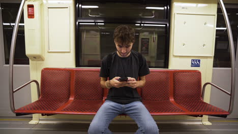 man sitting on subway train, using phone while sitting on chair