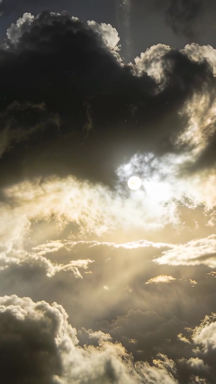 Video verticale: Brezza che sposta una grande nuvola scura rivelando un sole velato nel cielo al tramonto, proiettando raggi.