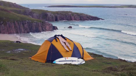 Surfer-Campen-In-Einem-Zelt-Oben-Auf-Der-Klippe-Mit-Blick-Auf-Einen-Kalten-Und-Zerklüfteten-Strand-Im-Schottischen-Hochland