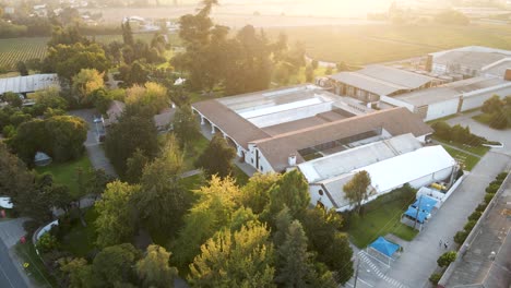 Tilt-down-aerial-view-of-the-facade-of-the-Undurraga-vineyard-in-Talagante,-Chile-with-the-sunset-in-the-background