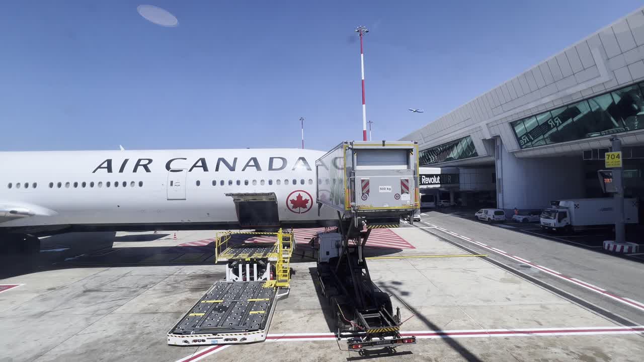 Air Canada plane stationed at airport gate with cargo loader and ground crew, preparing for loading or unloading on a clear, sunny day