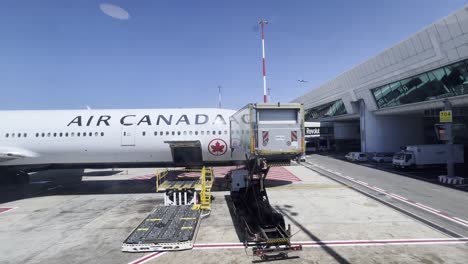 air canada plane stationed at airport gate with cargo loader and ground crew, preparing for loading or unloading on a clear, sunny day