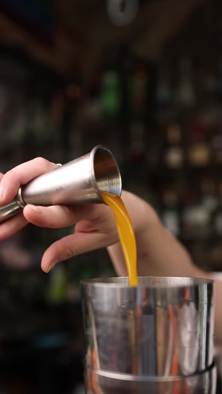 Barman che versa liquido giallo da un jigger in uno shaker per cocktail