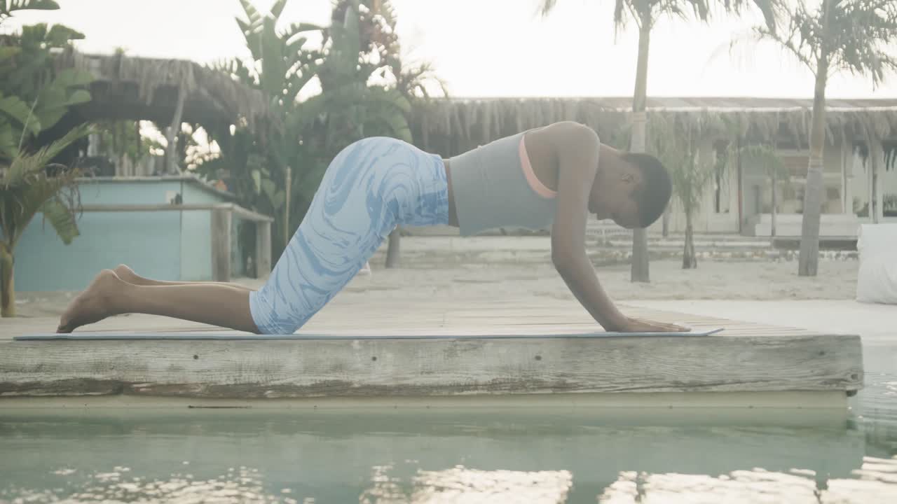 mujer biracial relajada practicando yoga, estirándose en la playa, cámara lenta