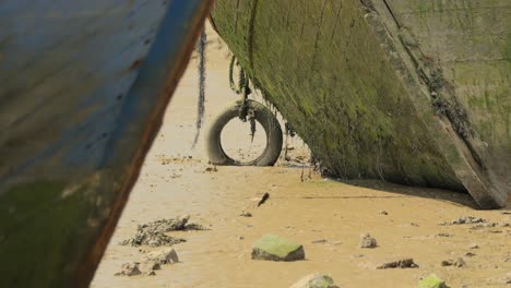 Hulls-of-beached-rotting-shipwrecks-with-old-tire-and-swaying-frayed-rope,-with-slow-zoom-out