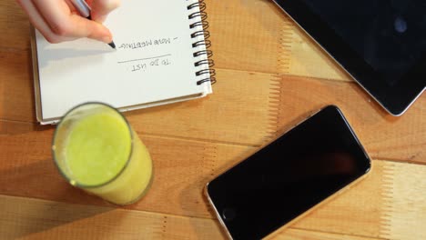 Hand of businesswoman writing on notebook at desk with glass of juice and mobile phone on table