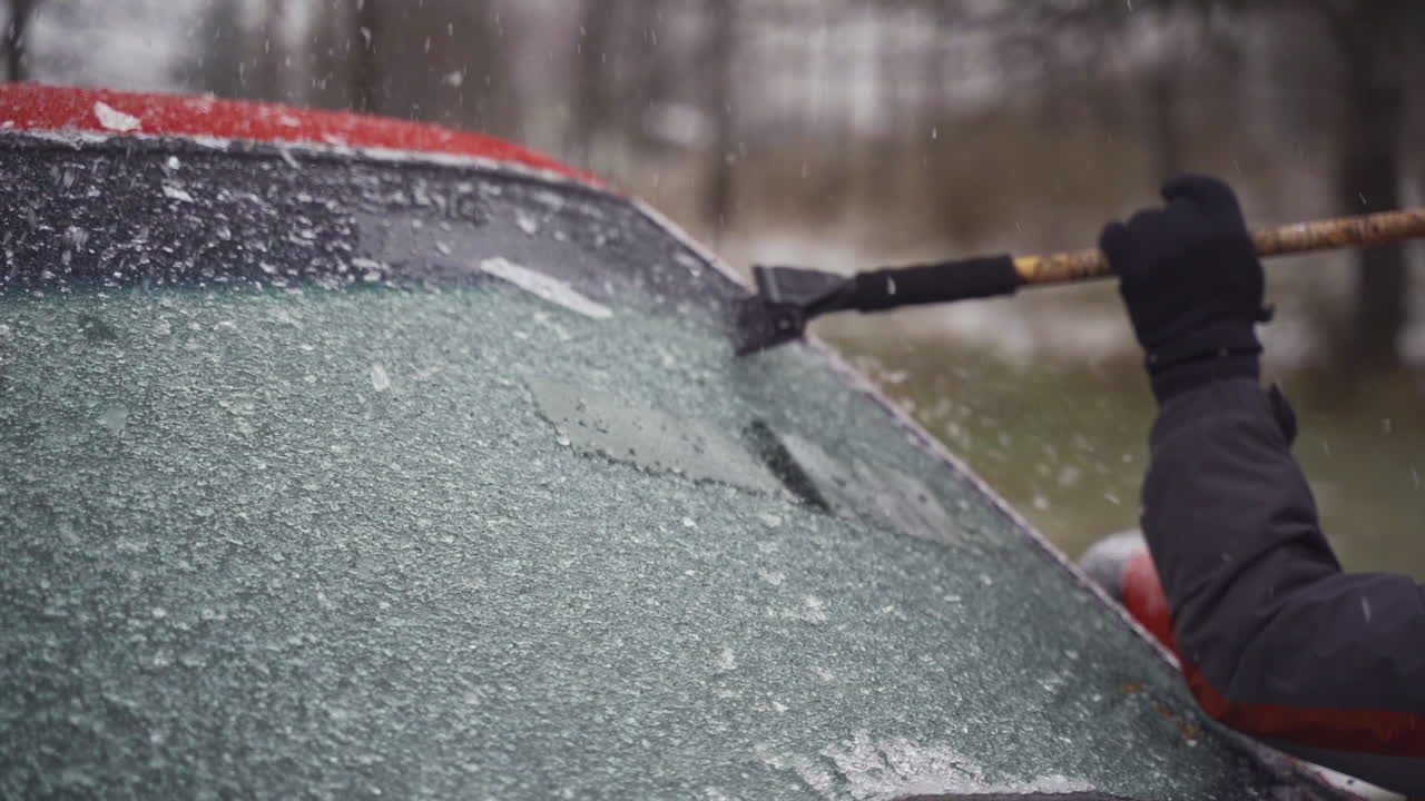 Man cleaning and scraping ice from car windshield in snow slowmo