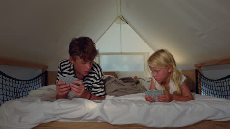 brother and sister playing cards in a tent at night