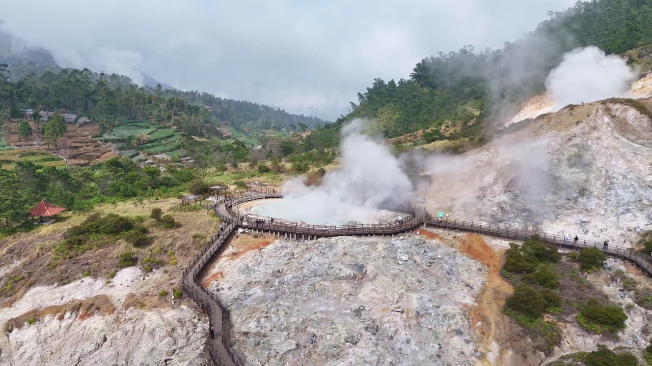 Aerial footage of Sikidang Crater in Dieng Plateau, Central Java, Indonesia, showing geothermal steam vents, volcanic landscape, and wooden walking paths surrounded by green hills