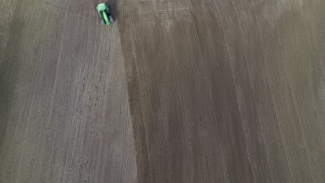 overhead aerial footage of a tractor coming into frame plowing field and then leaving frame at the bottom