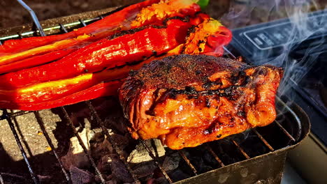 juicy grilled steak with charred red peppers cooking on a charcoal grill outdoors