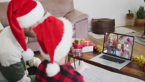 Caucasian-father-and-son-wearing-santa-hats-on-laptop-video-chat-during-christmas-at-home