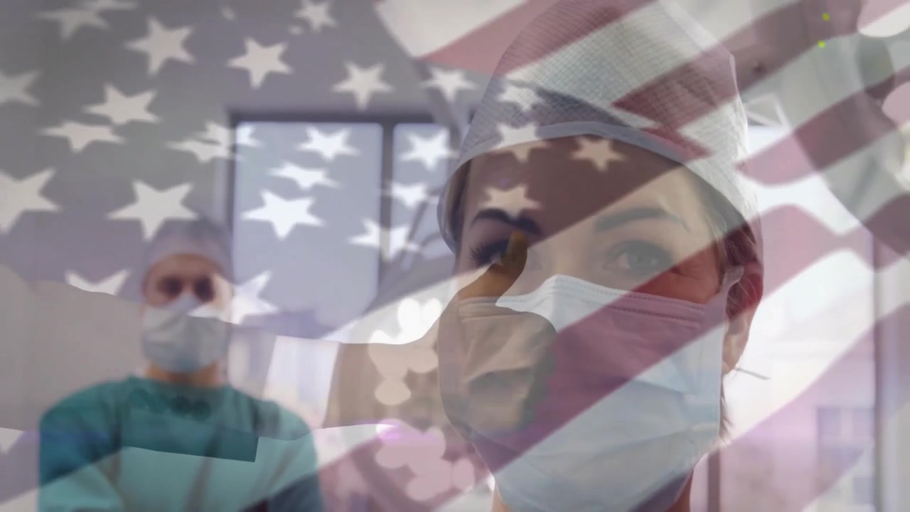 Healthcare worker lowering sleeve giving gloved thumbs-up for vaccine prep with US flag overlay