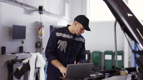 portrait of mechanic uses a laptop while conducting diagnostics test on engine