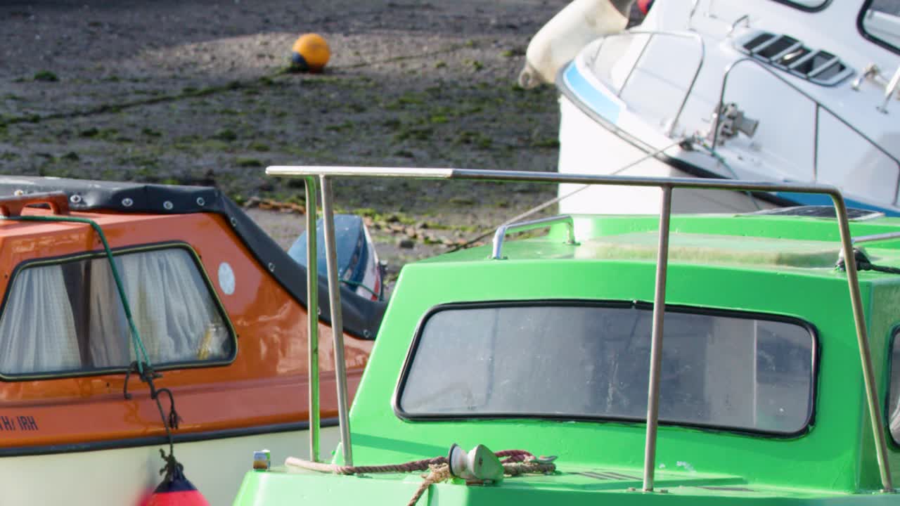 Green, orange, and white motorboats rest closely together in bright daylight, minimal camera movement