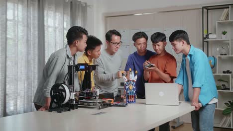 asian man with a laptop, 3d printing, and a cyborg hand teaching the boys fixing the circuit board at school