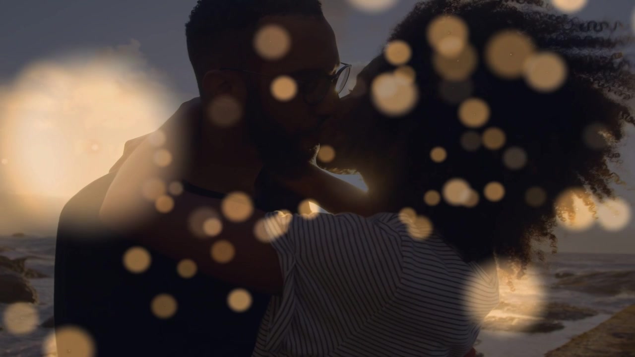 Vertical video: Man holding woman and kissing on rocky beach, moving bokeh revealing romance