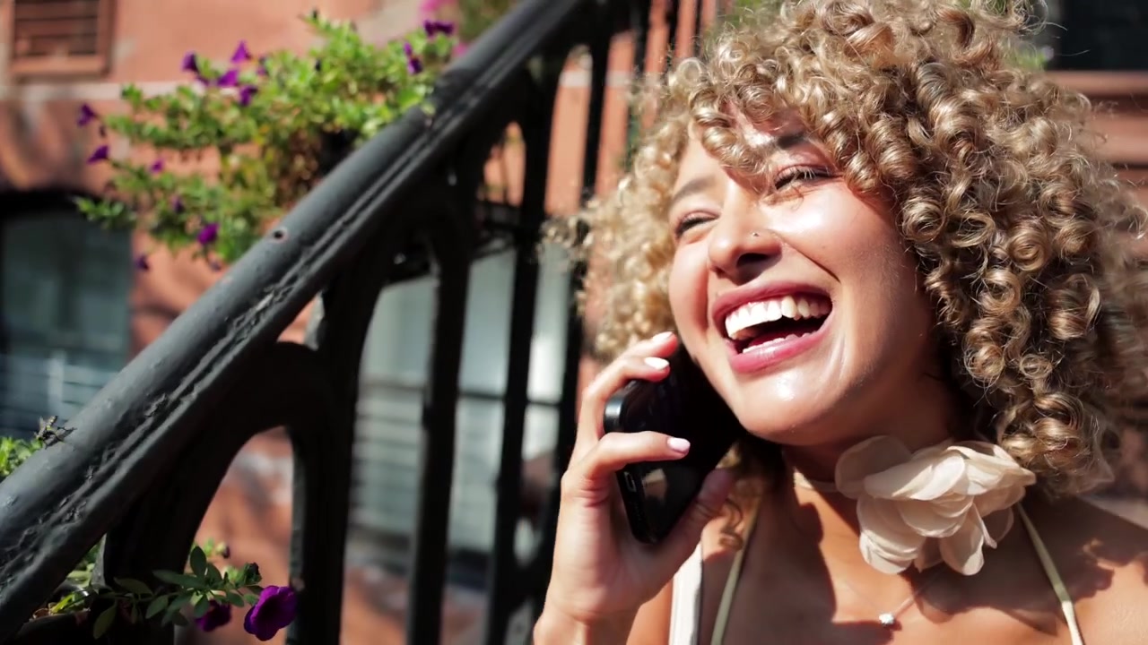 Giovane donna che ride mentre parla al telefono sui gradini di arenaria