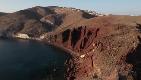 Luftaufnahme-Der-Griechischen-Küste-Und-Des-Roten-Strandes-Der-Insel-Santorini-An-Einem-Sonnigen-Abend,-Drohnenaufnahme