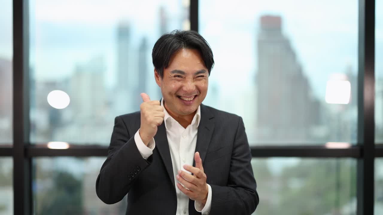 Asian businessman in formal suit claps and smiles, natural daylight, cityscape office background, static shot