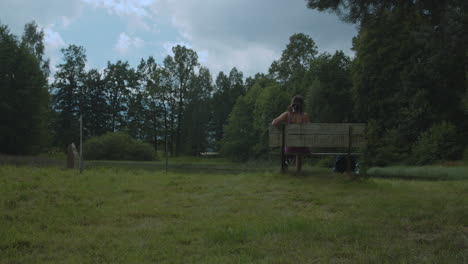 Girl-in-dress-sits-on-an-old-bench-by-pond-in-the-park