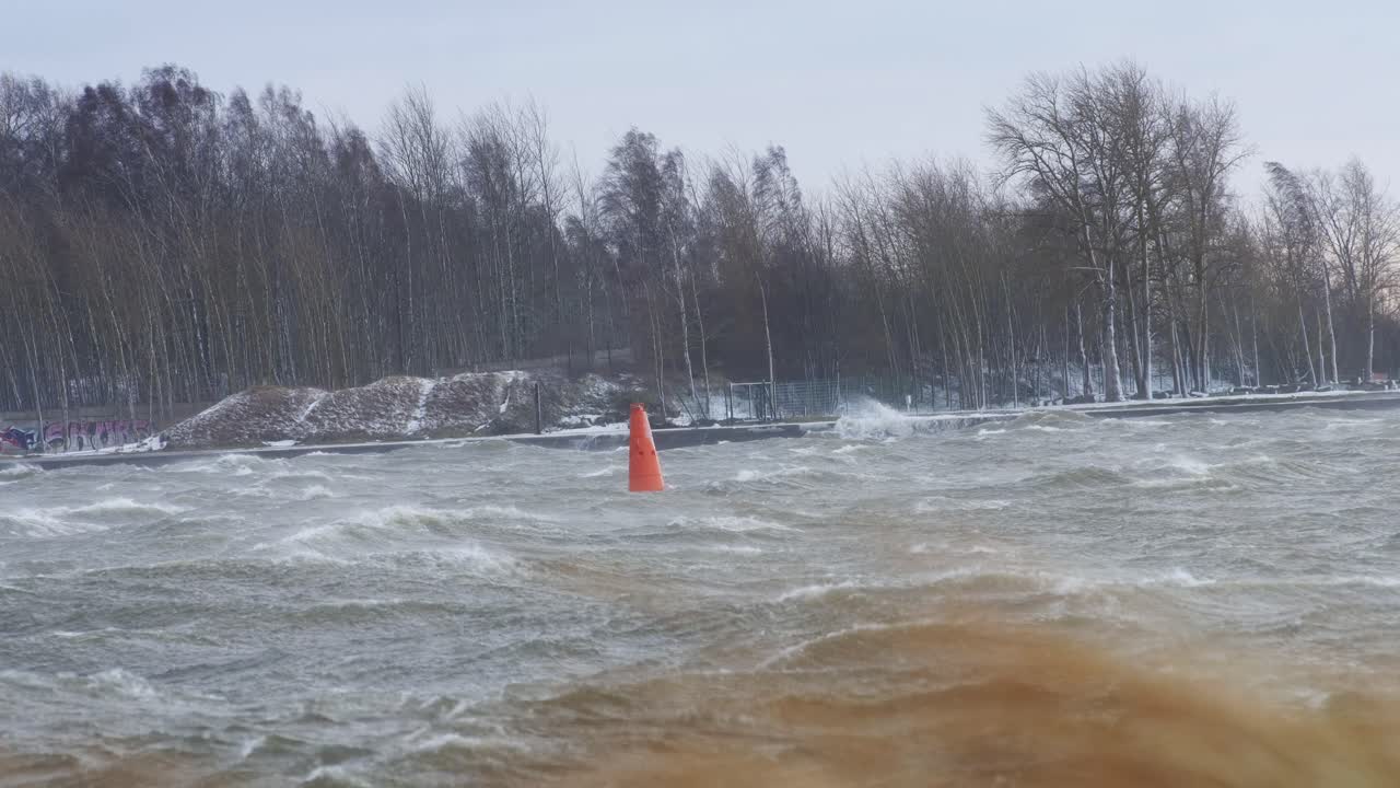 A lone orange buoy sways violently in stormy waters as waves crash around it