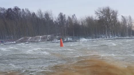 a lone orange buoy sways violently in stormy waters as waves crash around it
