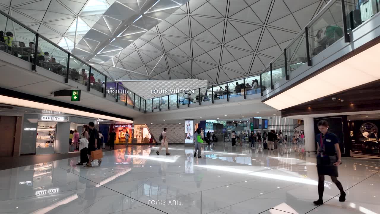 Busy scene of passengers walking past shops in the modern lower concourse at Hong Kong Airport, showcasing global travel and commercial activity.