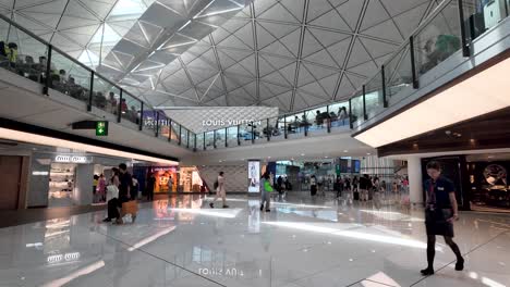 busy scene of passengers walking past shops in the modern lower concourse at hong kong airport, showcasing global travel and commercial activity.
