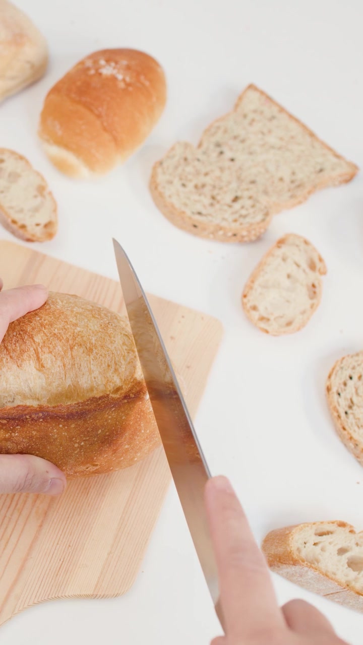 Close-up overhead shot of hands slicing crusty bread with a knife on a wooden board.