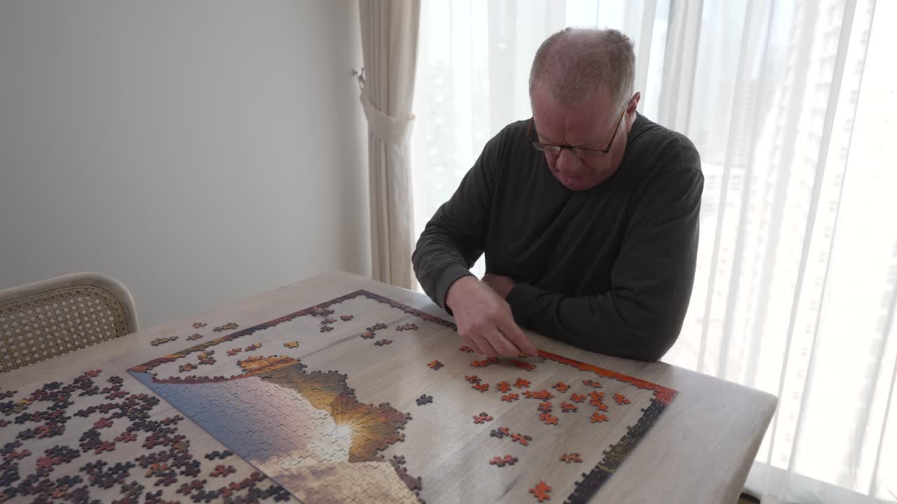 Elderly, retired man works on a picture puzzle at home to pass time