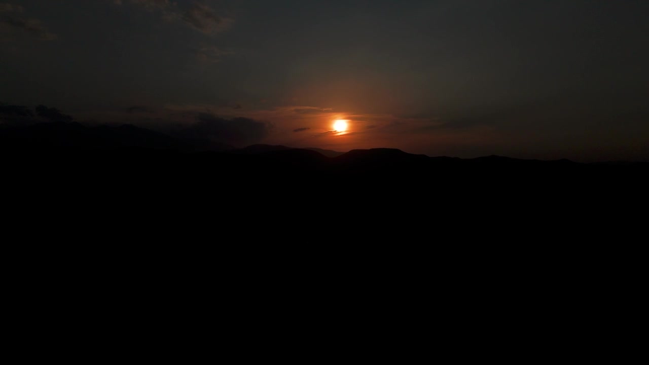 Toma estática de un eclipse solar parcial brillando sobre montañas silueteadas al anochecer