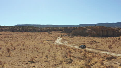 aerial of 4x4 car driving across open desert landscape on dirt road, 4k