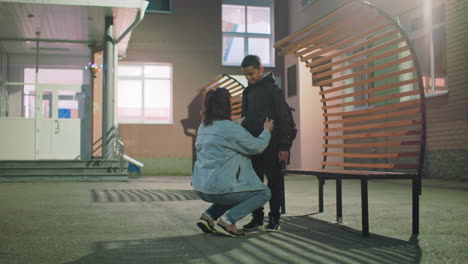 Woman standing near school entrance gently adjusts boy’s backpack and clothes during early morning before classes, showing care and support, with warm lighting and urban background