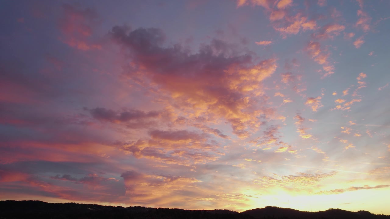 El dron captura un cielo matutino tranquilo, pintado en tonos azules y rosados. La luz toca las nubes, creando una vista serena mientras el horizonte brilla con la promesa de un nuevo día