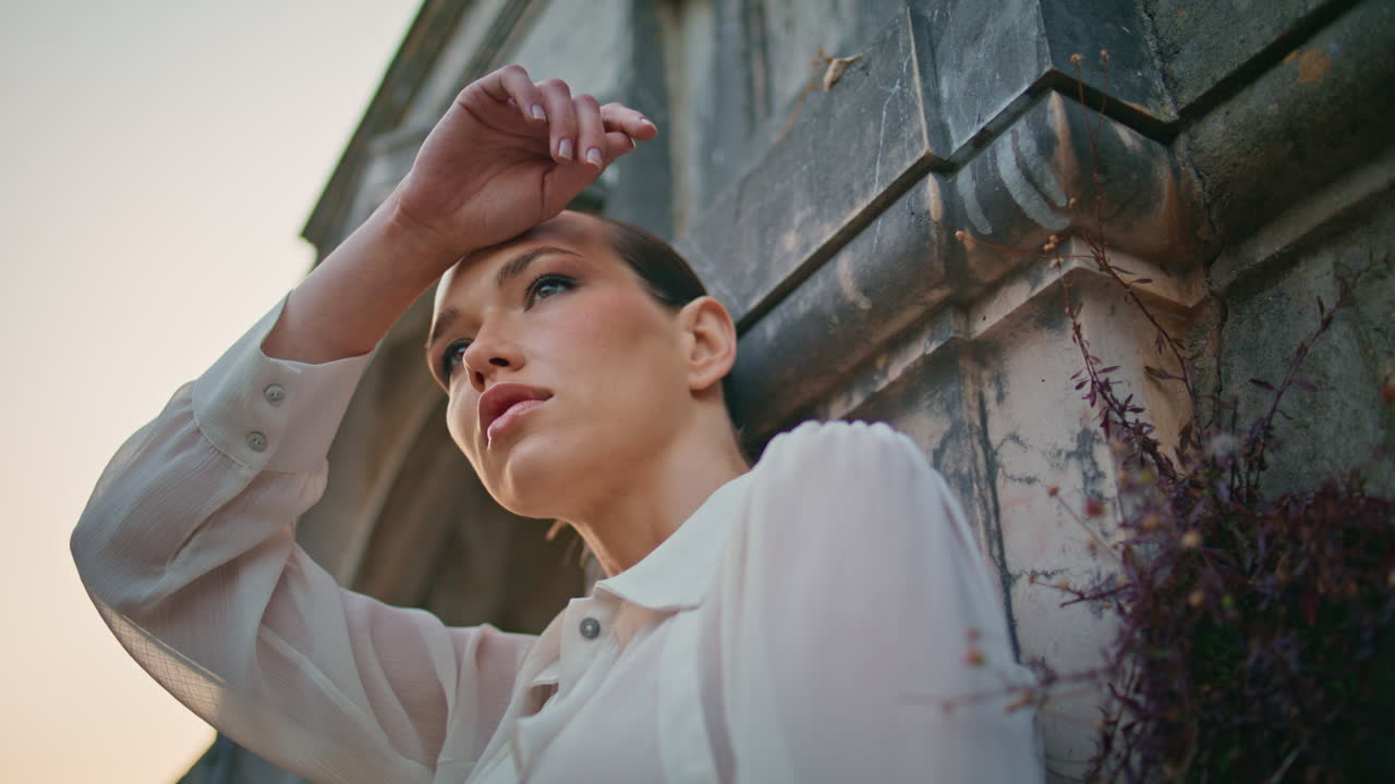 매력적인 모델을 찾는 카메라가 중세 벽에 머리를 올려서 손을 들어 올립니다.