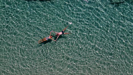 aerial top view over romantic happy couple floating in crystal clear waters, paros