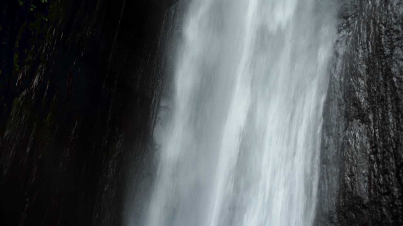 Close-up, tilt-up detail shot of Munduk Waterfall, Bali. Showcases the power and beauty of the cascading water, highlighting the textures and details of the falls.