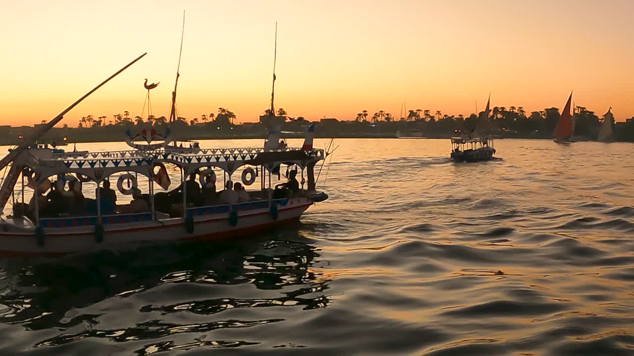 River scape of Tourists sitting on egyption Local felucca tour boats on Nile river Crossing from west to east bank with sunset colors reflecting on water. Luxor, Egypt