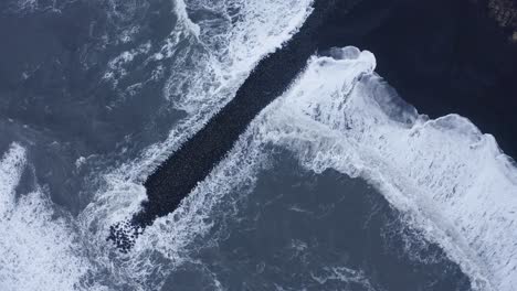 Ascending-drone-top-down-of-extreme-ocean-waves-flooding-basalt-rocks-and-black-beach-in-Iceland