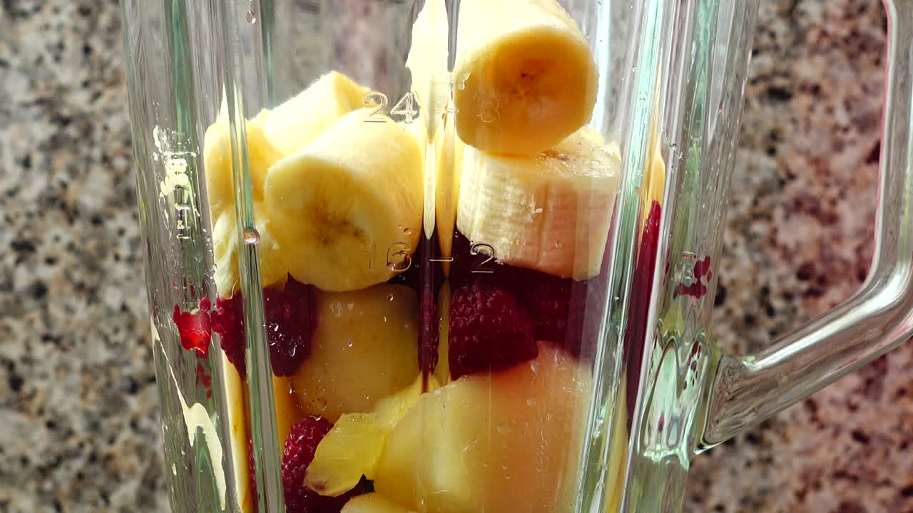 Fyller blenderen med biter av pære, bringebær og bananer