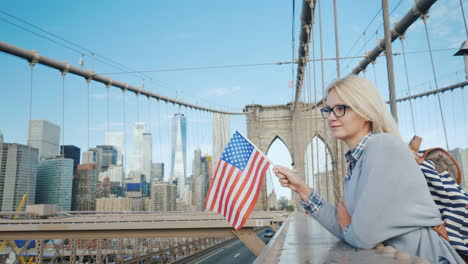 a woman with the flag of america in her hand stands on the brooklyn bridge with a view of manhattan