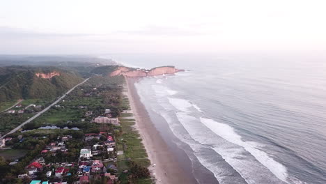 vista aérea del mar en calma salpicando a la orilla con casas y árboles verdes en la playa de olon, ecuador - toma aérea