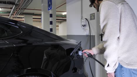 Hombre-Conectando-El-Cargador-A-Un-Coche-Eléctrico-En-Un-Aparcamiento-Subterráneo