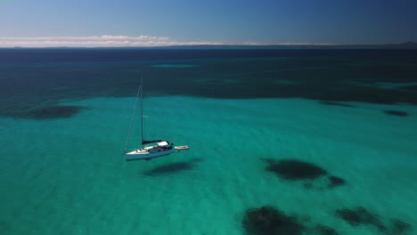 Sailboat-anchored-in-small-cove-off-private-tropical-island,-New-Caledonia